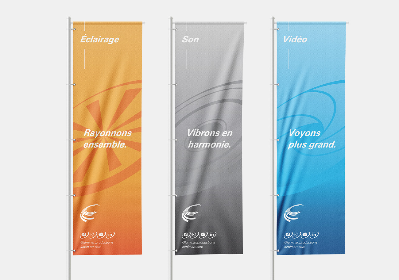 Trois drapeaux publicitaires verticaux pour Lumin-ART Productions – design d'identité visuelle moderne et dynamique, motifs abstraits en rayons de lumière et ondes concentriques, déclinaison tricolore orange/gris/bleu par pôle de service (éclairage, son, vidéo), typographie manuscrite élégante en italique